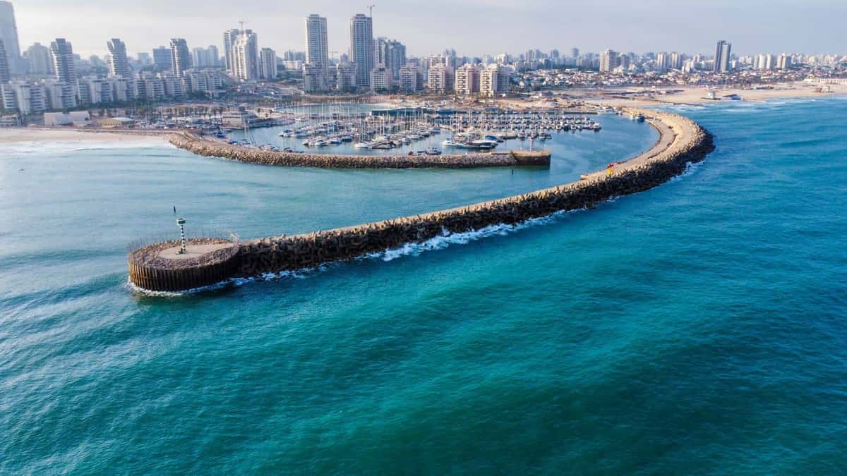 מבט מהאוויר על מרינה אשדוד: שובר הגלים, סירות המפרש העוגנות ומגדלי המגורים של העיר לחוף הים התיכון